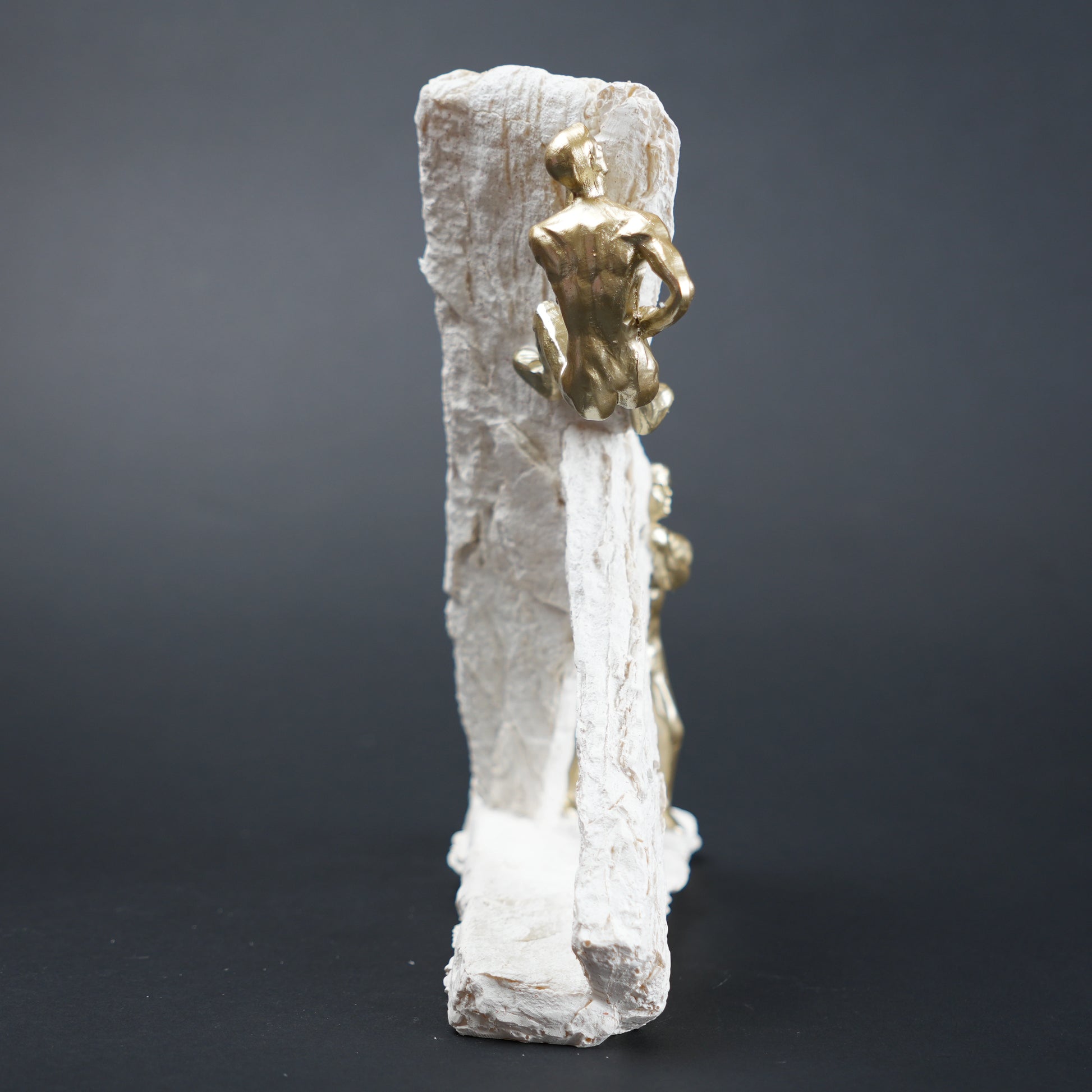Gold figurine on a white rock-like structure against a dark background