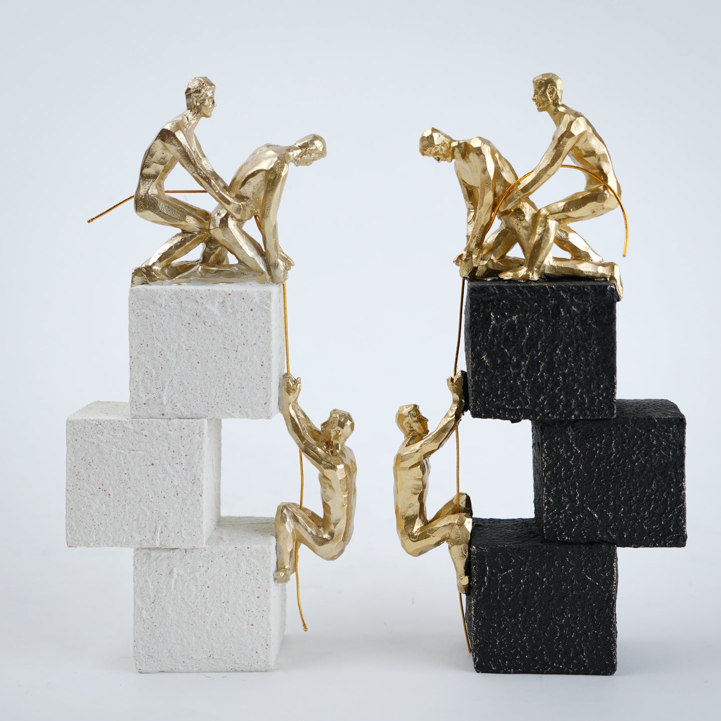 Gold sculptures of people climbing on stacked blocks against a white background