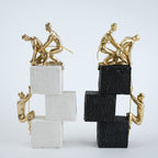 Two gold sculpture figures on stacked black and white blocks against a light gray background