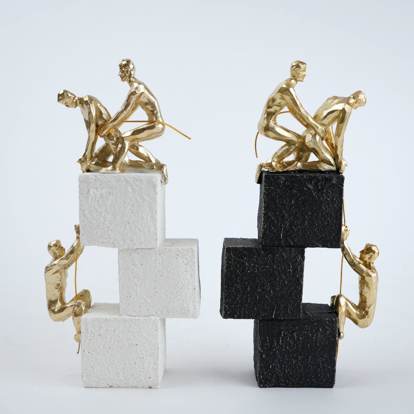 Two gold sculpture figures on stacked black and white blocks against a light gray background