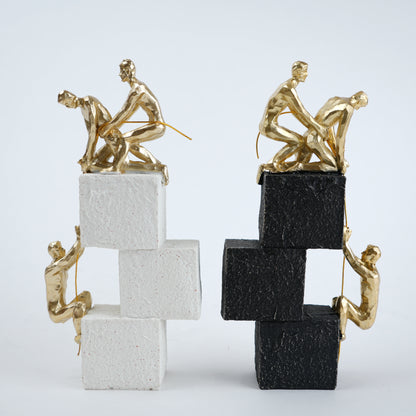 Two gold sculpture figures on stacked black and white blocks against a light gray background