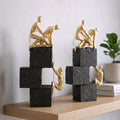 Two gold sculpture figures on stacked black and white blocks against a light gray background
