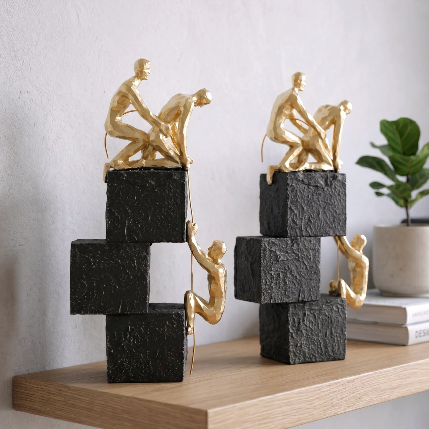 Two gold sculpture figures on stacked black and white blocks against a light gray background