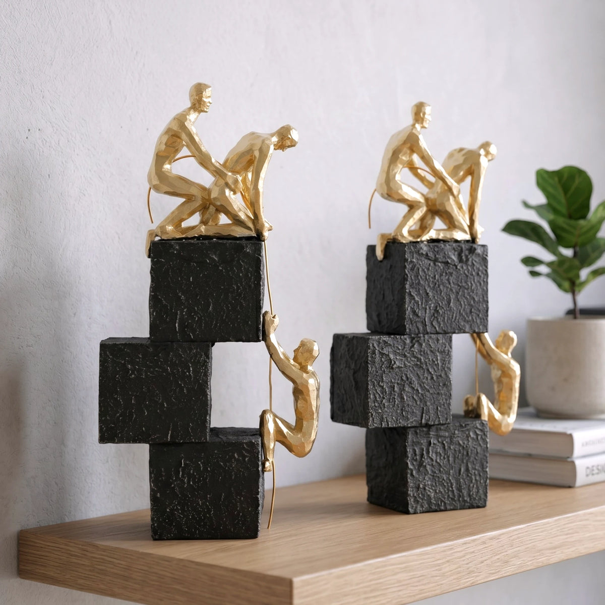 Two gold sculpture figures on stacked black and white blocks against a light gray background