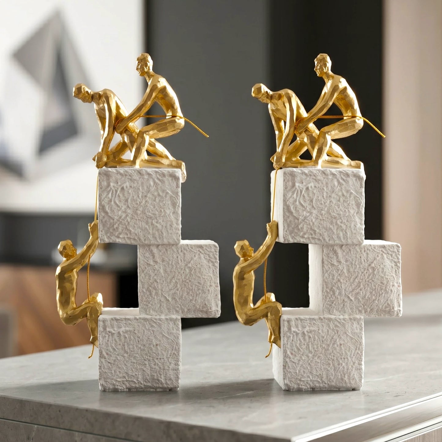 Two gold sculpture figures on stacked black and white blocks against a light gray background