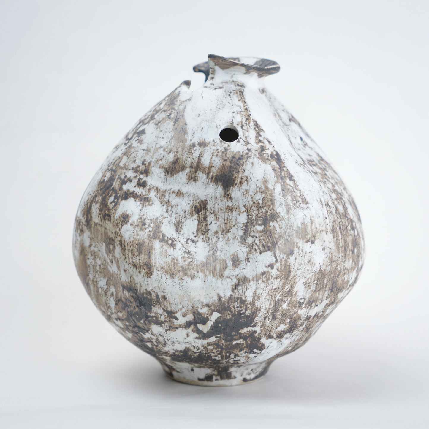 White distressed ceramic vase with rounded body and narrow base, featuring a textured rustic finish, dual side openings, and an uneven top rim, ideal for modern home decor and artistic styling.