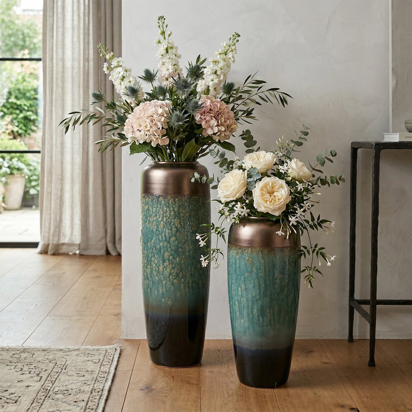 Two tall ceramic vases with floral arrangements on a wooden floor.