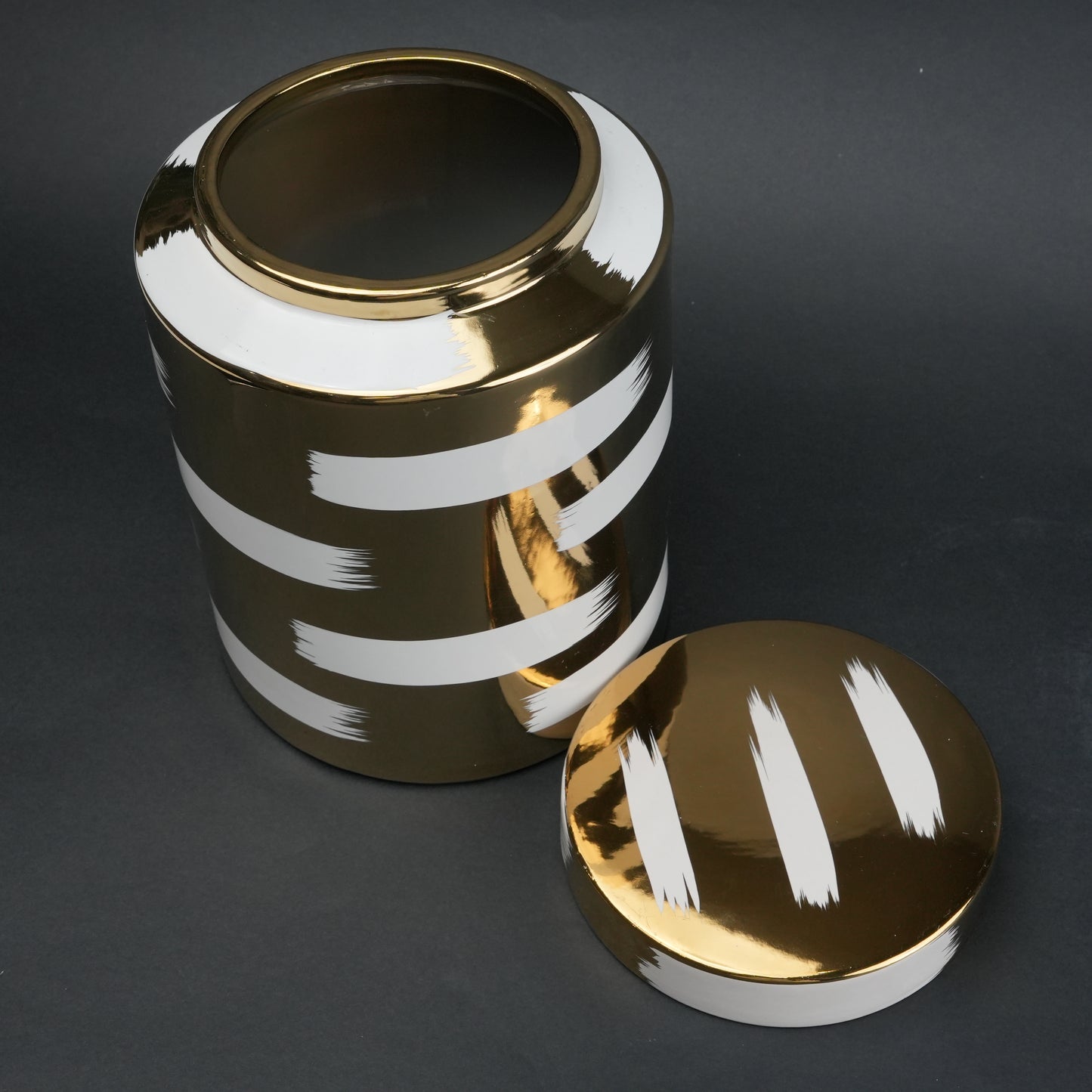 Gold decorative metal jar with white brushstroke design and matching lid