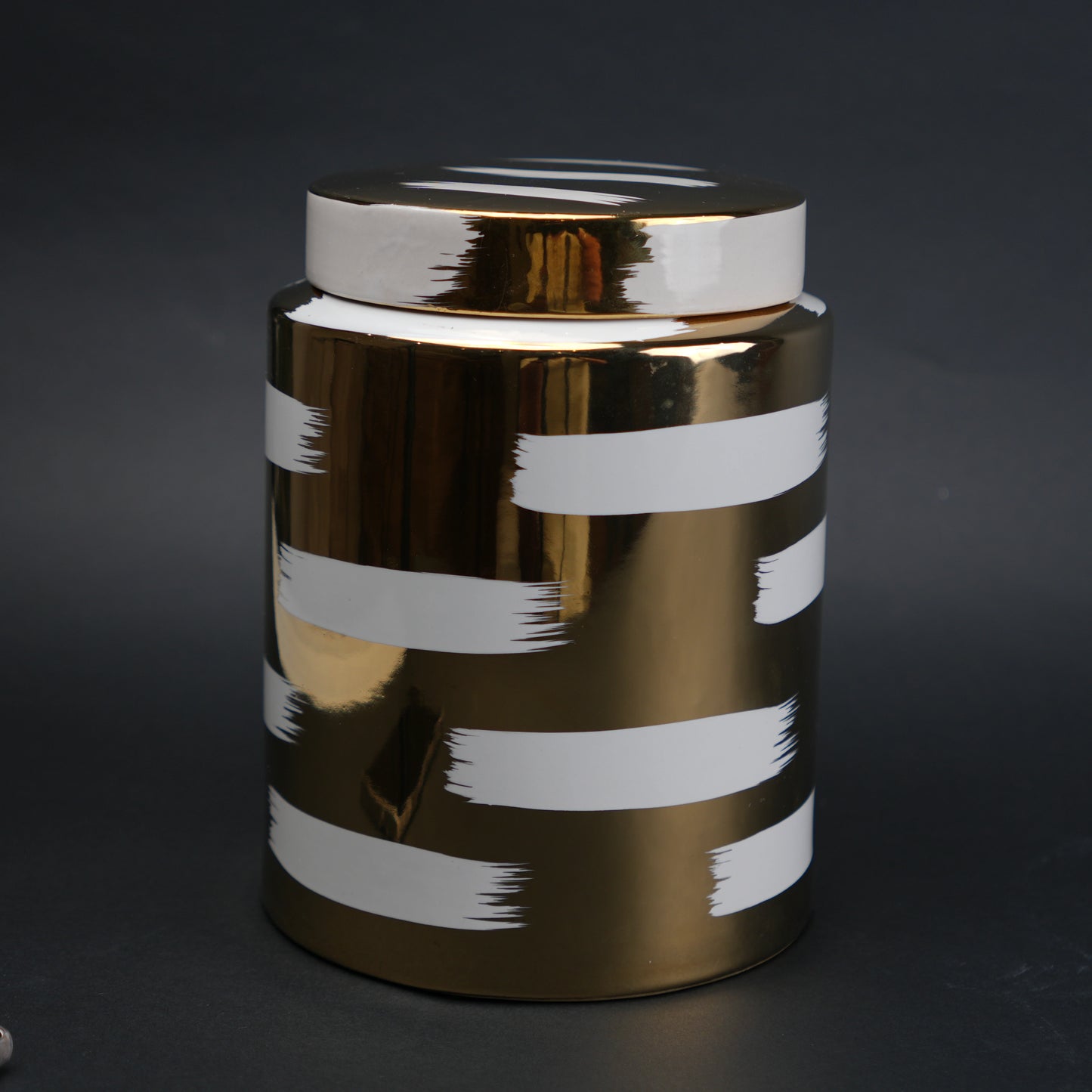 Gold decorative metal jar with white brushstroke design and matching lid