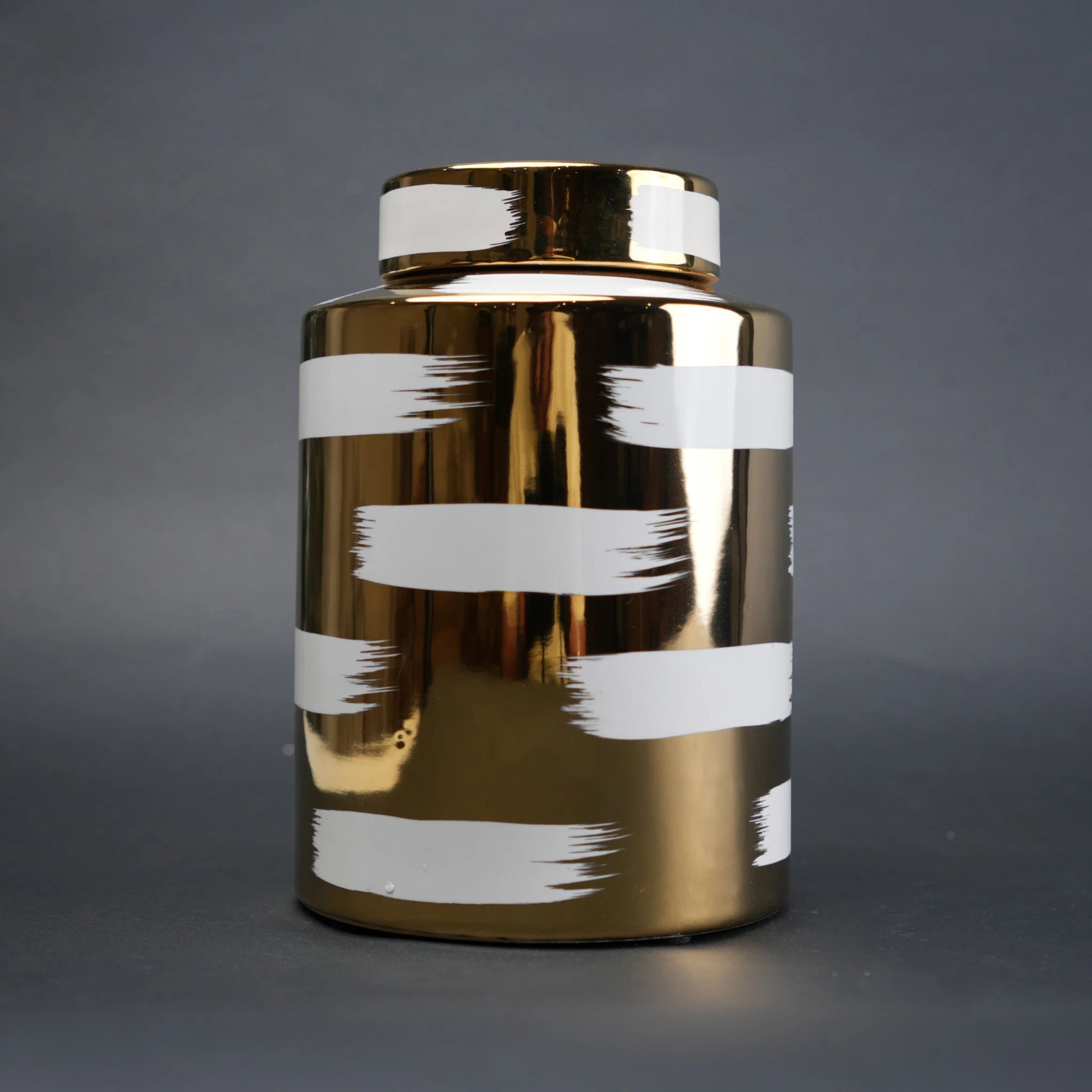Gold decorative metal jar with white brushstroke design and matching lid