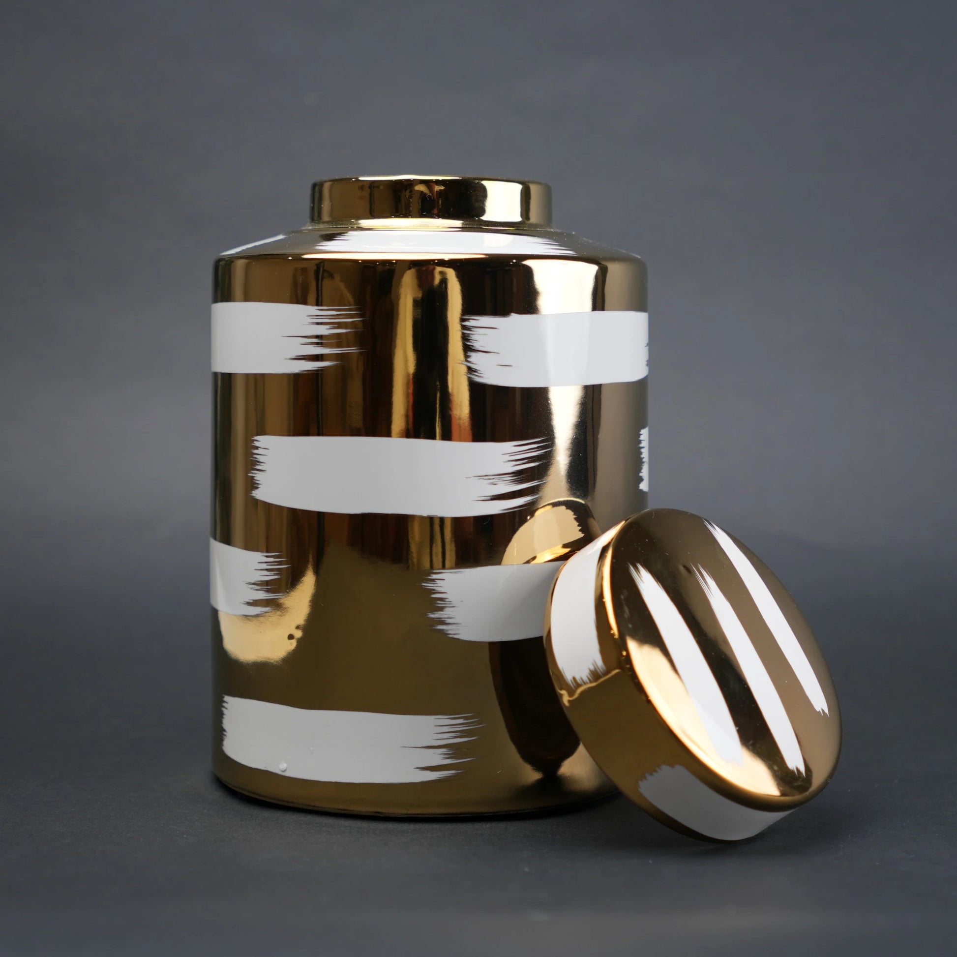 Gold decorative metal jar with white brushstroke design and matching lid