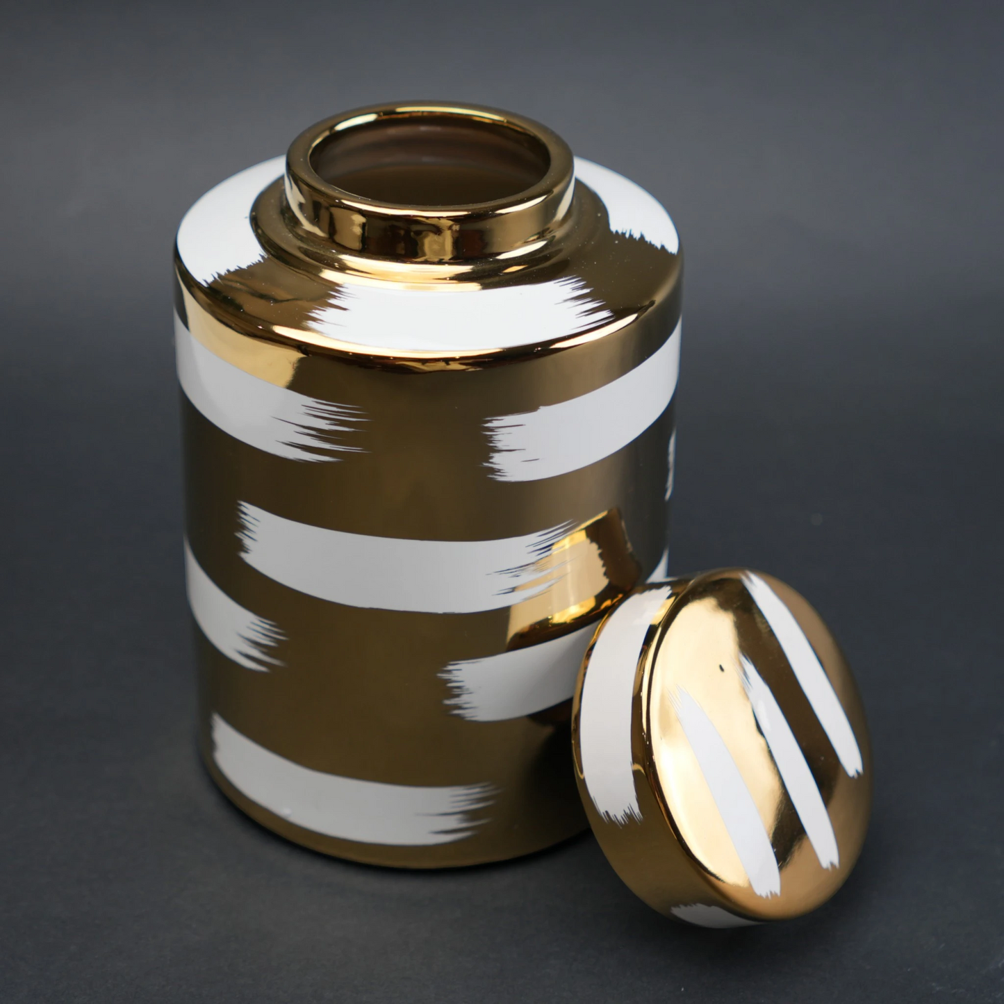 Gold decorative metal jar with white brushstroke design and matching lid