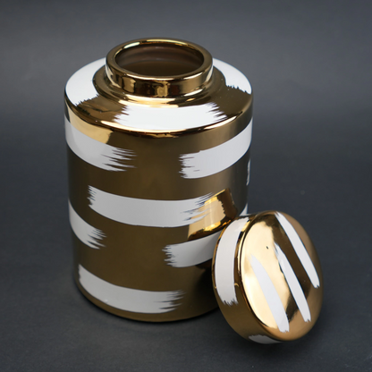 Gold decorative metal jar with white brushstroke design and matching lid