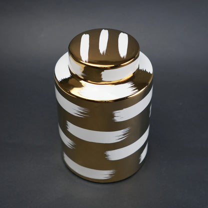 Gold decorative metal jar with white brushstroke design and matching lid