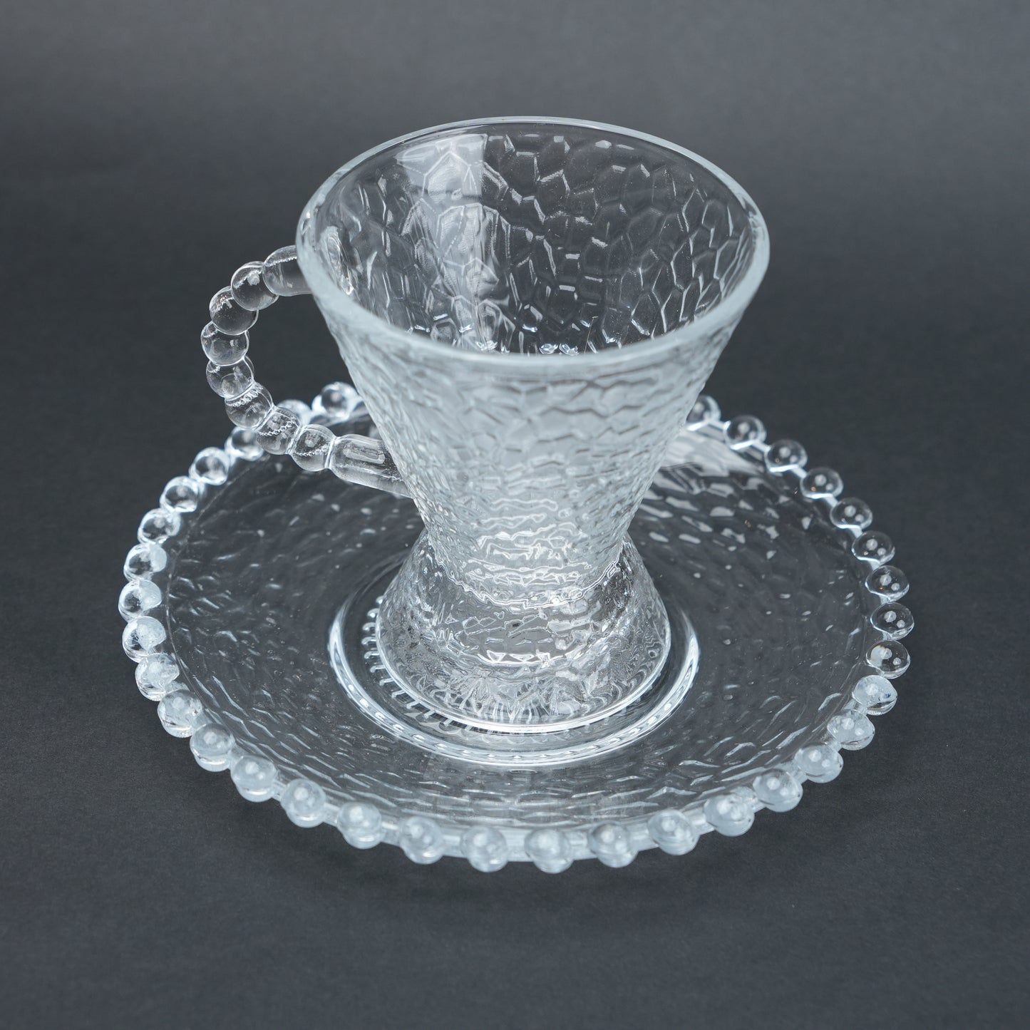 clear textured glass flared tea cup and saucer set with beaded handle for modern table setting