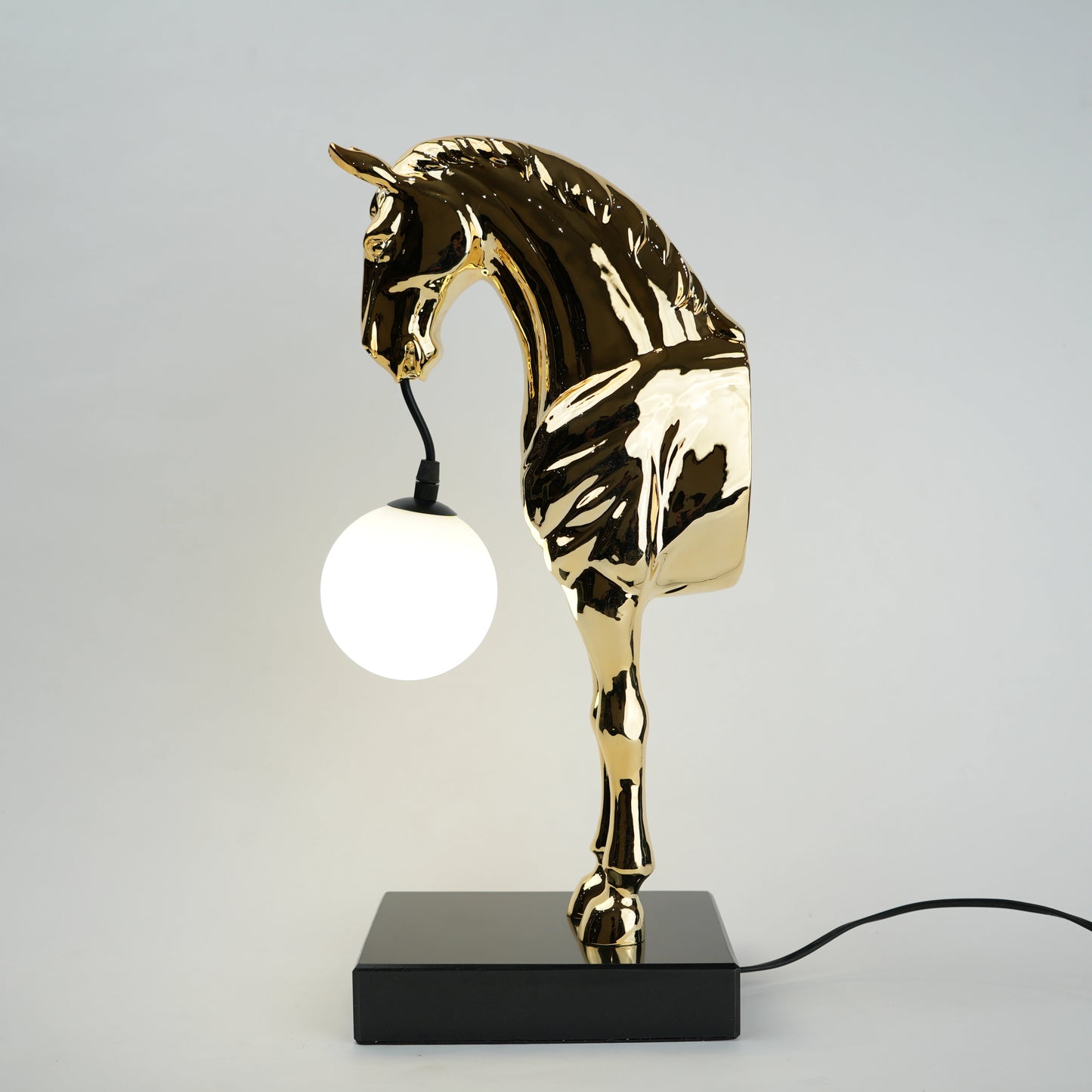 Golden horse table lamp with a sculpted horse base holding a frosted spherical globe light, featuring a smooth metallic finish and a structured base designed for soft ambient lighting and decorative use.