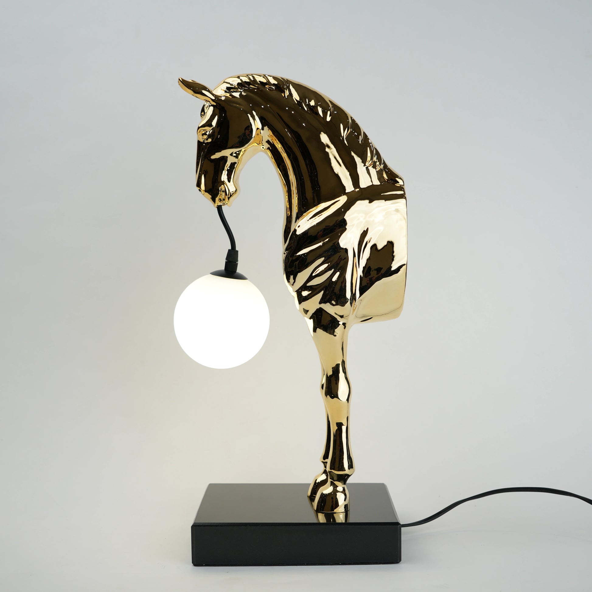 Golden horse table lamp with a sculpted horse base holding a frosted spherical globe light, featuring a smooth metallic finish and a structured base designed for soft ambient lighting and decorative use.