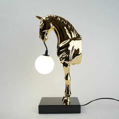 Golden horse table lamp with a sculpted horse base holding a frosted spherical globe light, featuring a smooth metallic finish and a structured base designed for soft ambient lighting and decorative use.