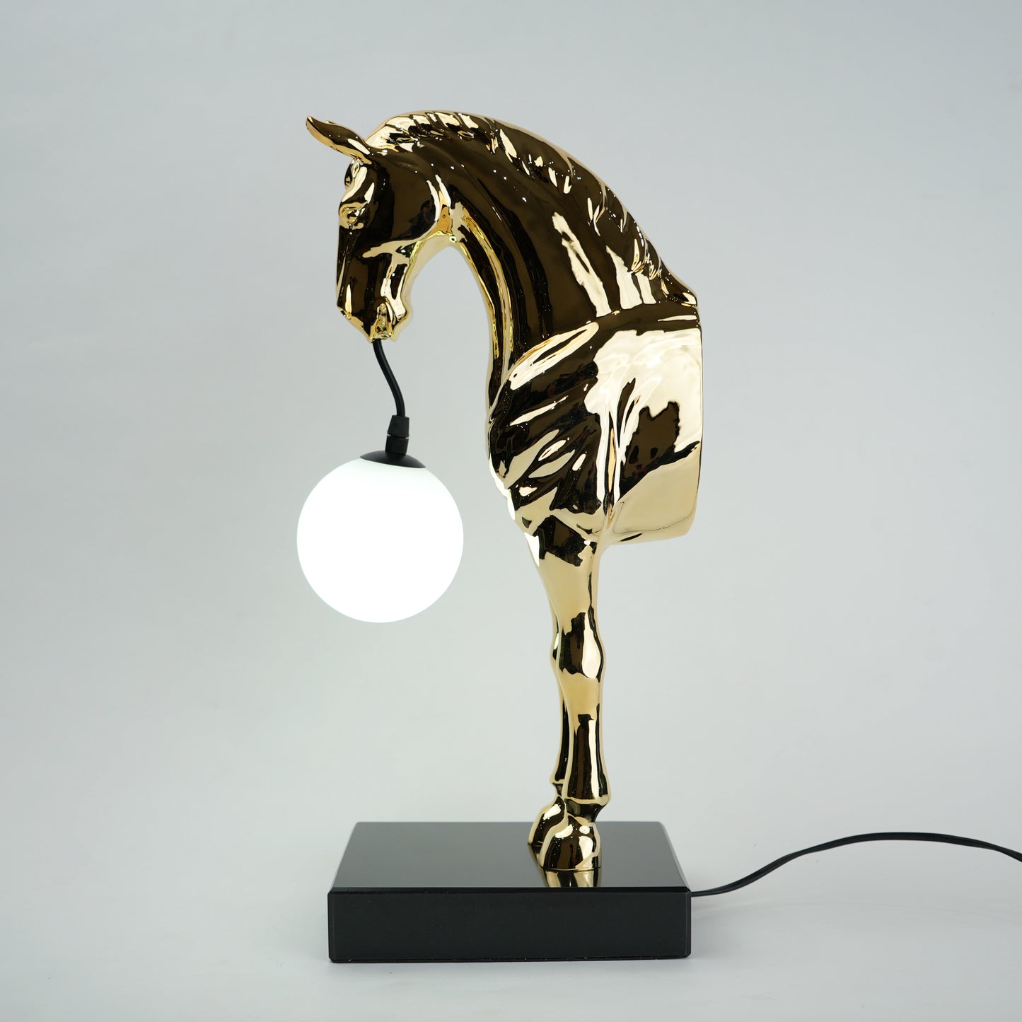 Golden horse table lamp with a sculpted horse base holding a frosted spherical globe light, featuring a smooth metallic finish and a structured base designed for soft ambient lighting and decorative use.
