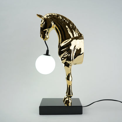 Golden horse table lamp with a sculpted horse base holding a frosted spherical globe light, featuring a smooth metallic finish and a structured base designed for soft ambient lighting and decorative use.