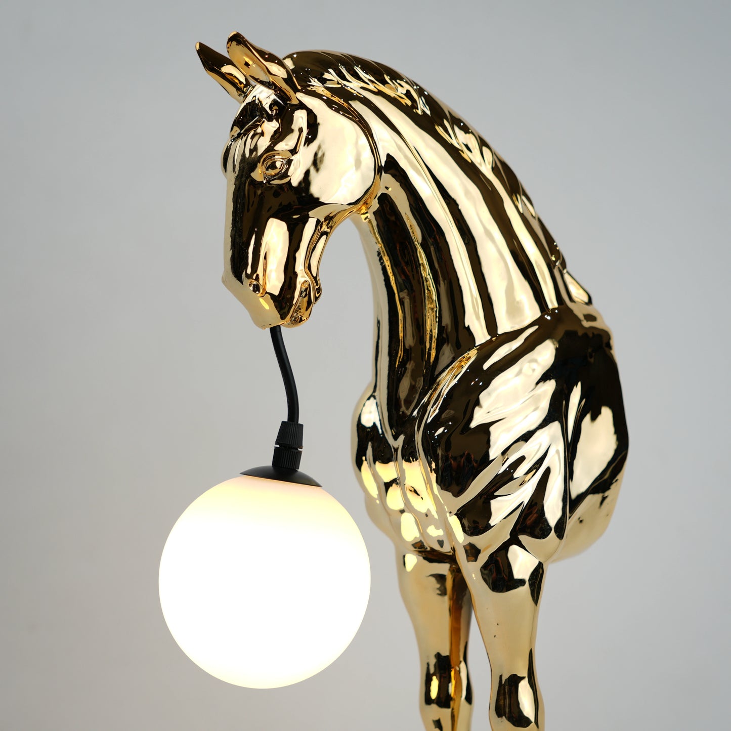 Golden horse table lamp with a sculpted horse base holding a frosted spherical globe light, featuring a smooth metallic finish and a structured base designed for soft ambient lighting and decorative use.