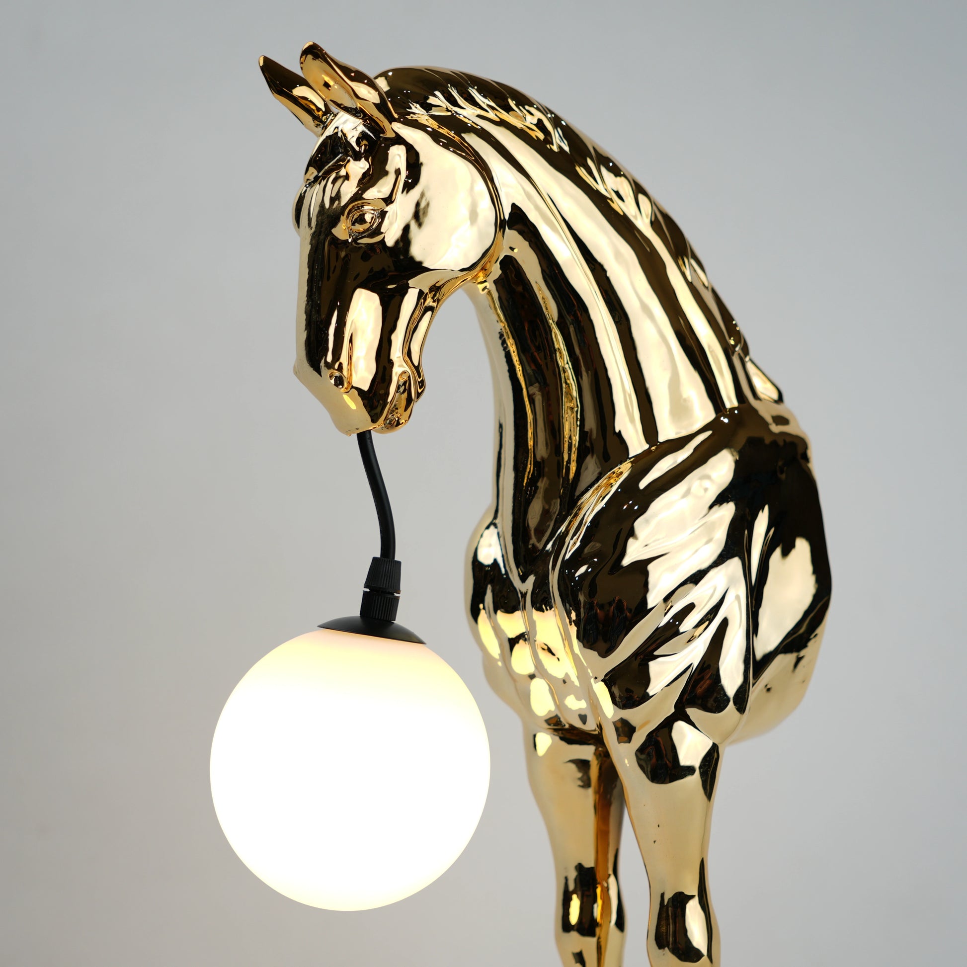 Golden horse table lamp with a sculpted horse base holding a frosted spherical globe light, featuring a smooth metallic finish and a structured base designed for soft ambient lighting and decorative use.