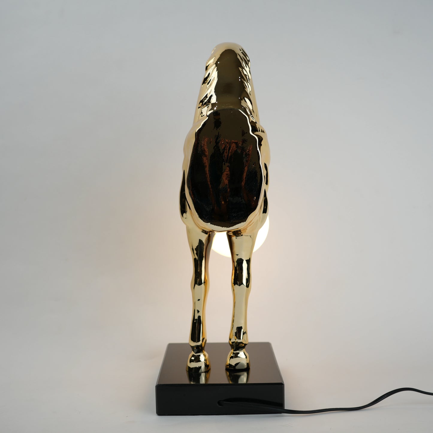 Golden horse table lamp with a sculpted horse base holding a frosted spherical globe light, featuring a smooth metallic finish and a structured base designed for soft ambient lighting and decorative use.