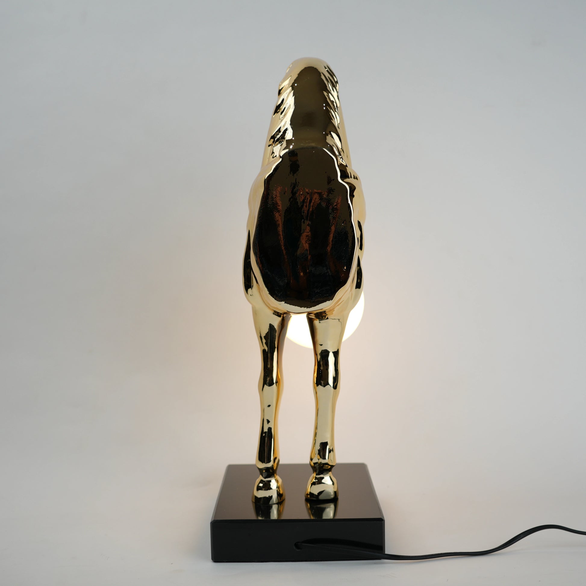 Golden horse table lamp with a sculpted horse base holding a frosted spherical globe light, featuring a smooth metallic finish and a structured base designed for soft ambient lighting and decorative use.
