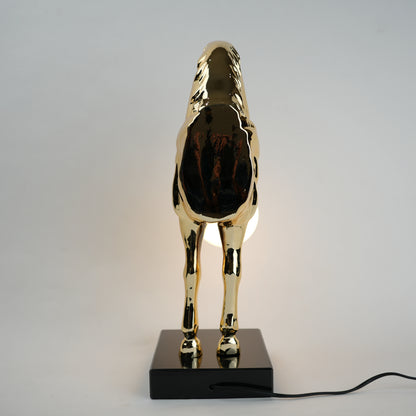 Golden horse table lamp with a sculpted horse base holding a frosted spherical globe light, featuring a smooth metallic finish and a structured base designed for soft ambient lighting and decorative use.