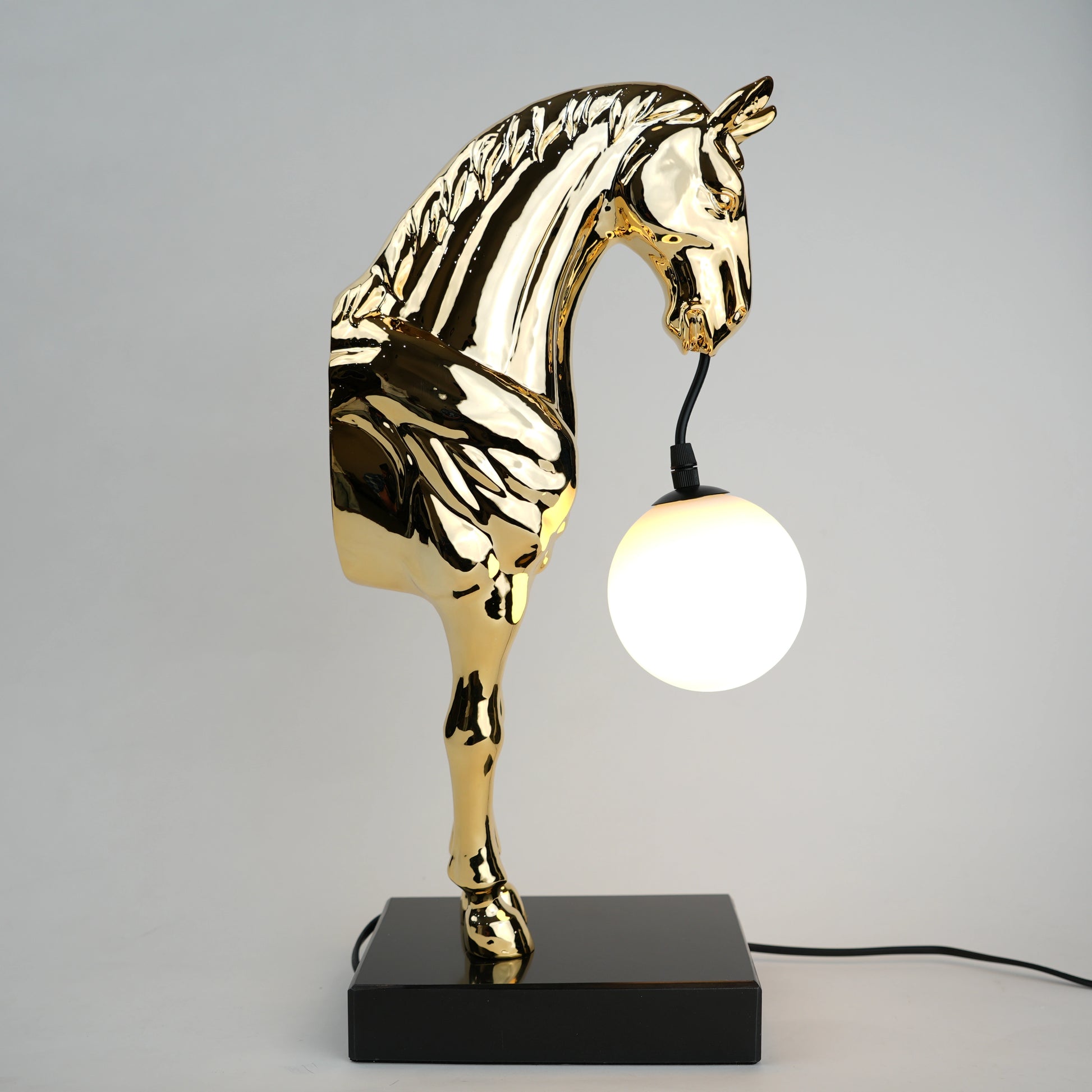 Golden horse table lamp with a sculpted horse base holding a frosted spherical globe light, featuring a smooth metallic finish and a structured base designed for soft ambient lighting and decorative use.