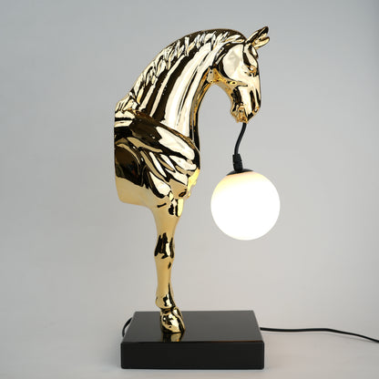 Golden horse table lamp with a sculpted horse base holding a frosted spherical globe light, featuring a smooth metallic finish and a structured base designed for soft ambient lighting and decorative use.
