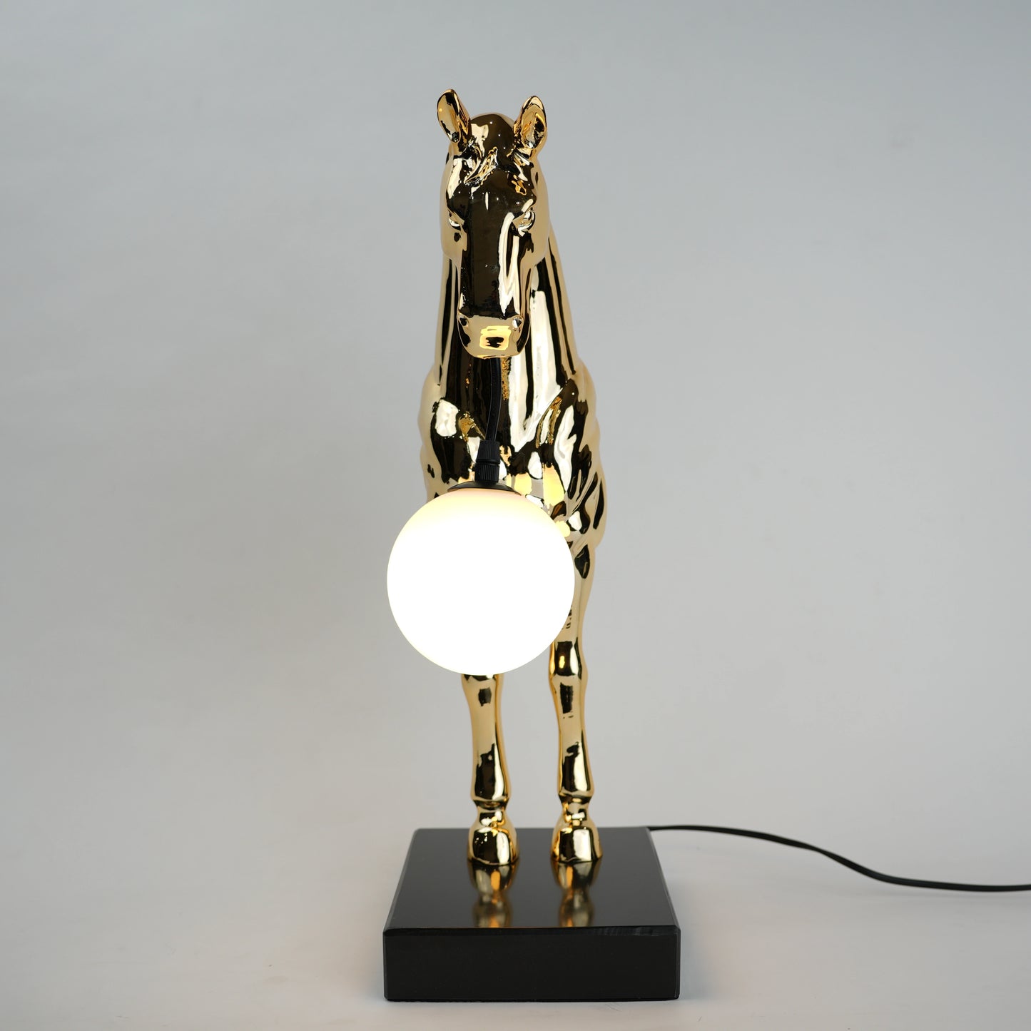 Golden horse table lamp with a sculpted horse base holding a frosted spherical globe light, featuring a smooth metallic finish and a structured base designed for soft ambient lighting and decorative use.