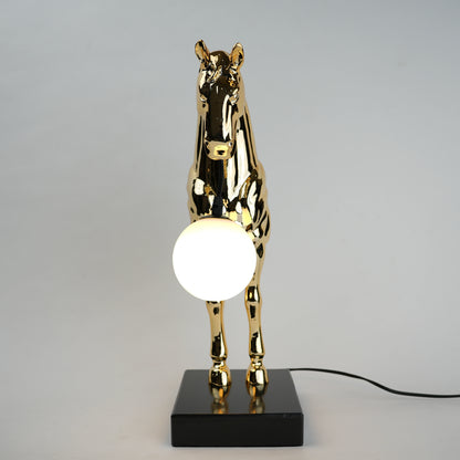 Golden horse table lamp with a sculpted horse base holding a frosted spherical globe light, featuring a smooth metallic finish and a structured base designed for soft ambient lighting and decorative use.
