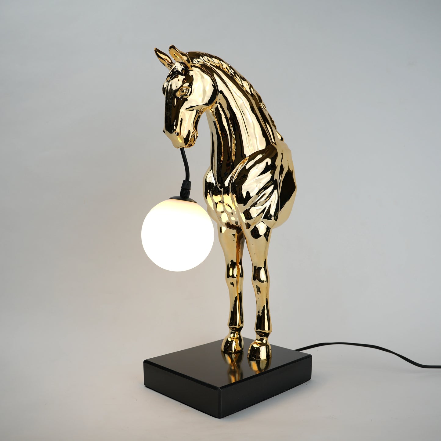 Golden horse table lamp with a sculpted horse base holding a frosted spherical globe light, featuring a smooth metallic finish and a structured base designed for soft ambient lighting and decorative use.