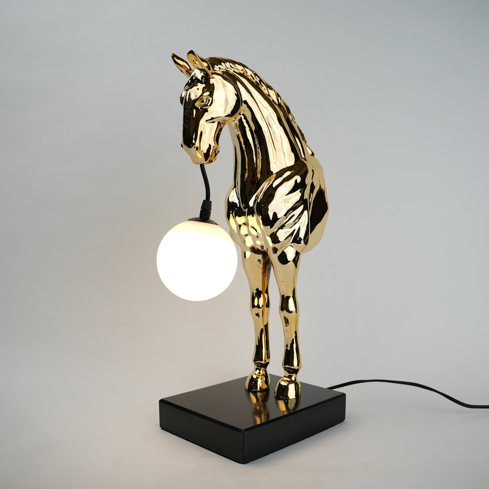 Golden horse table lamp with a sculpted horse base holding a frosted spherical globe light, featuring a smooth metallic finish and a structured base designed for soft ambient lighting and decorative use.