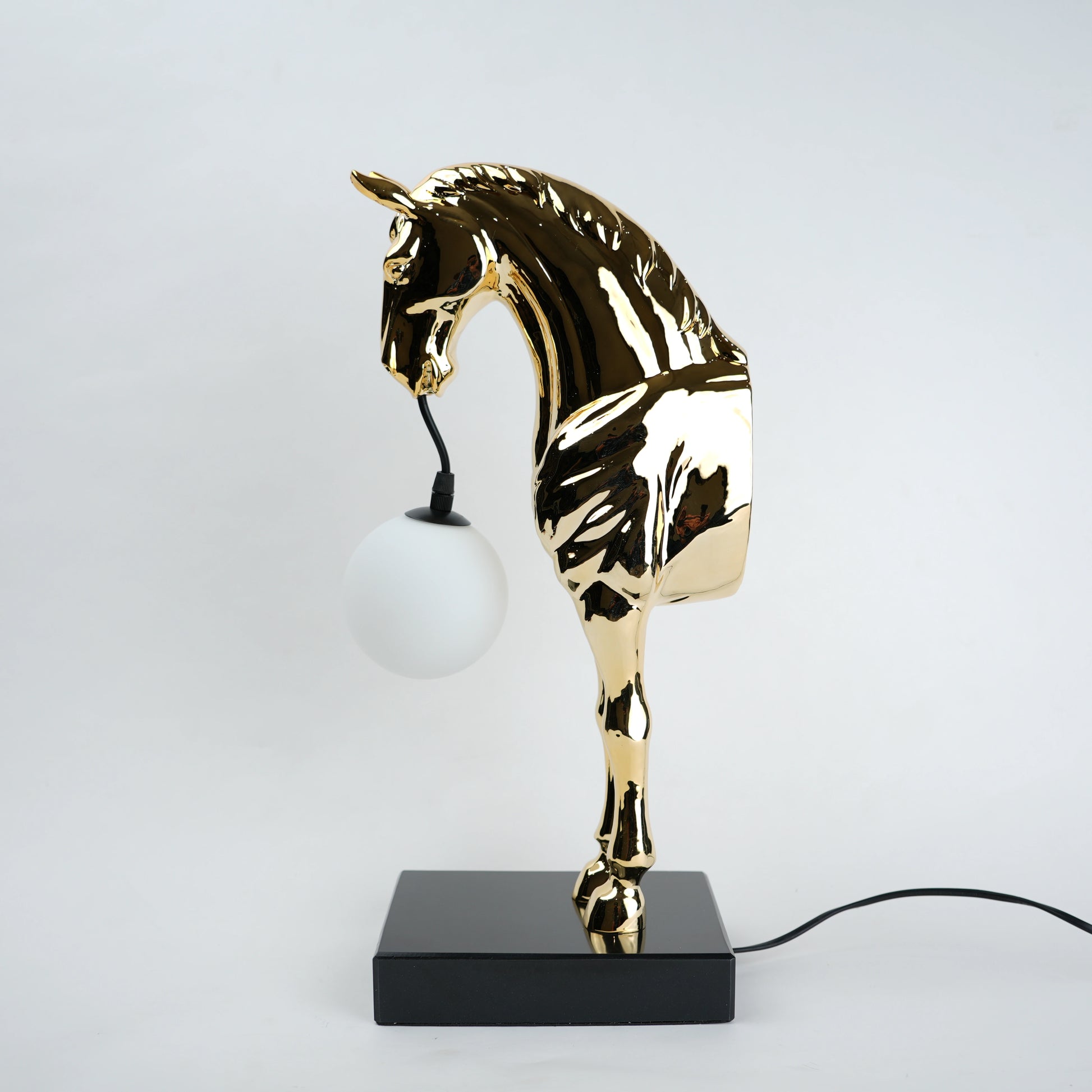 Golden horse table lamp with a sculpted horse base holding a frosted spherical globe light, featuring a smooth metallic finish and a structured base designed for soft ambient lighting and decorative use.