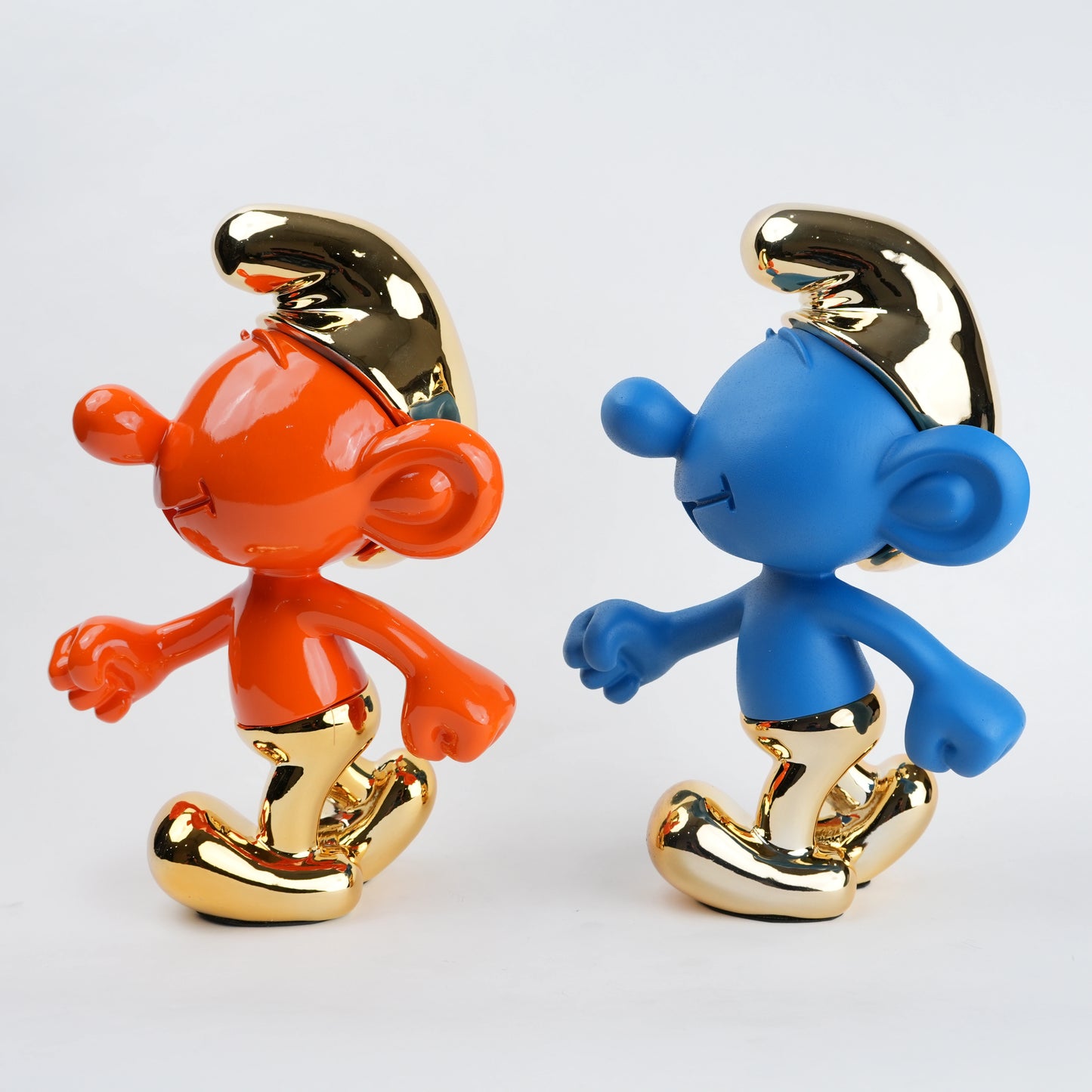 Two Smurf figurines, one orange and one blue, with gold accents on a light gray background.