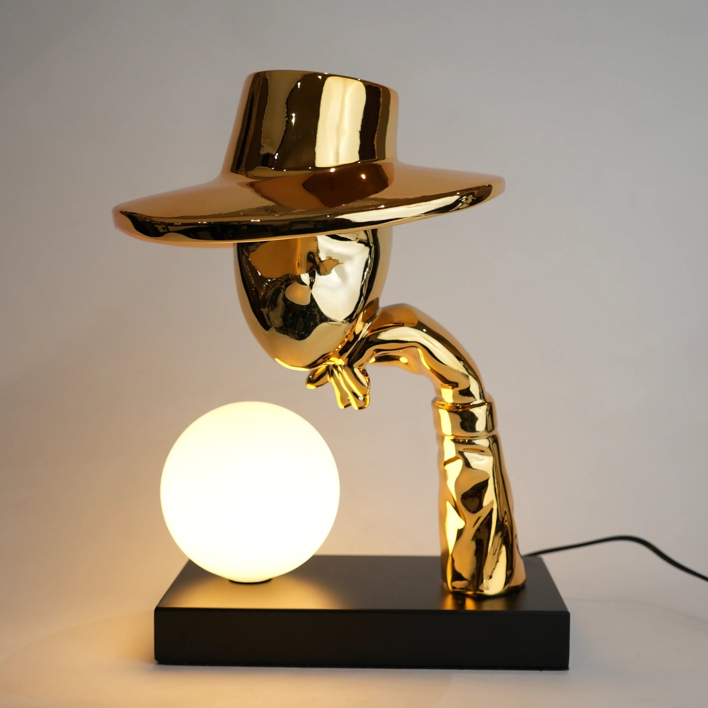 Gold lamp with a unique design on a black base against a gray background