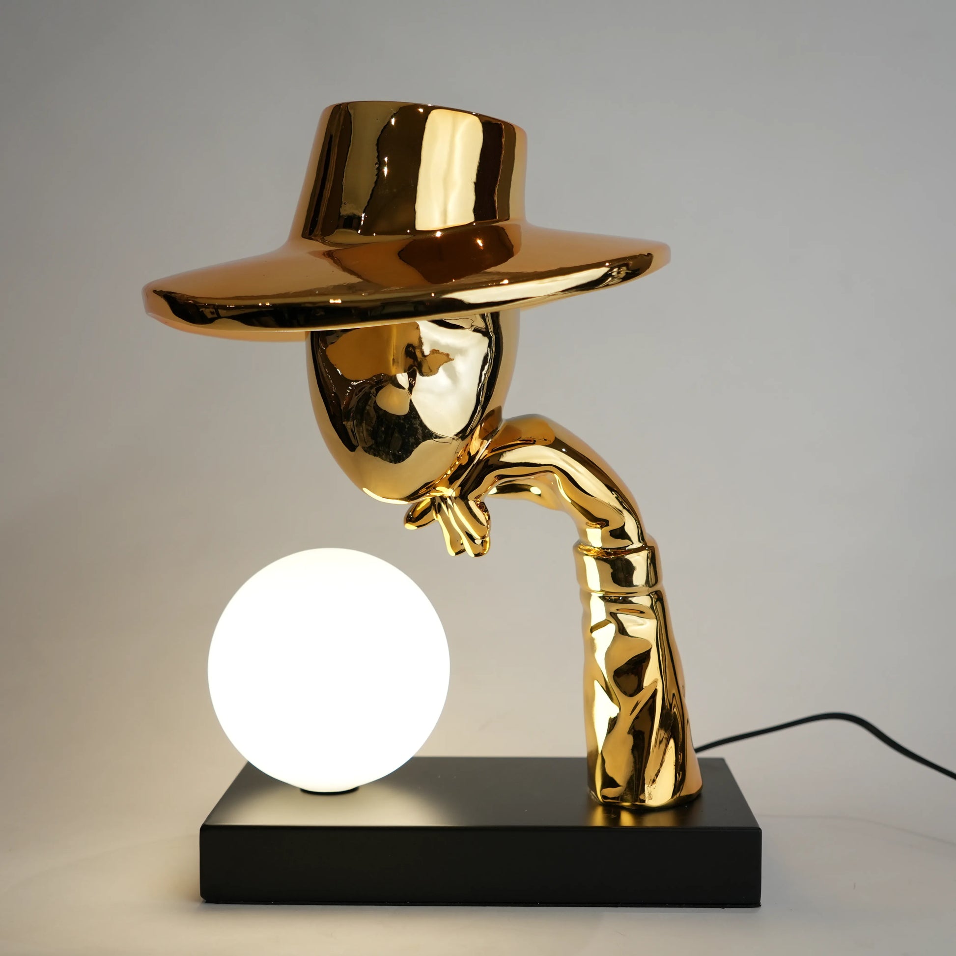 Gold lamp with a unique design on a black base against a gray background
