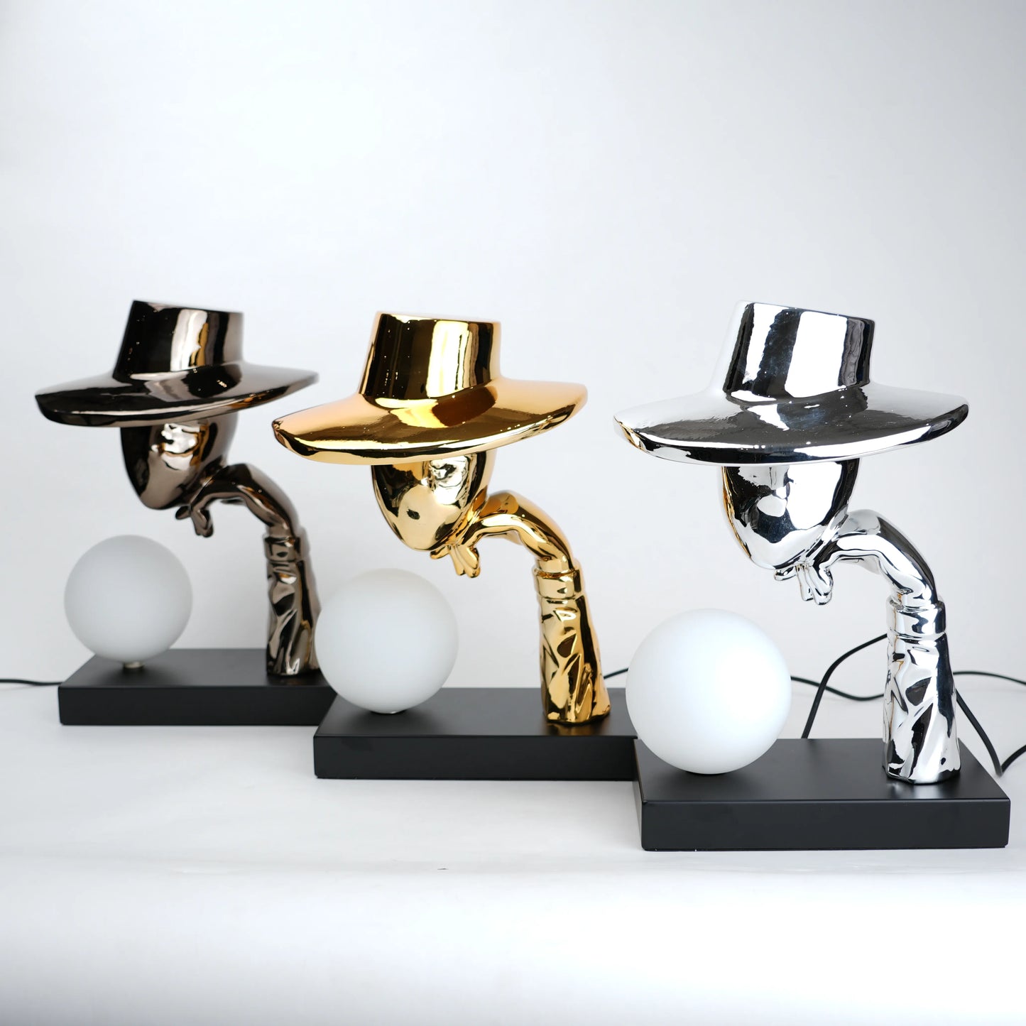 Three unique table lamps with metallic shades and black bases on a white background