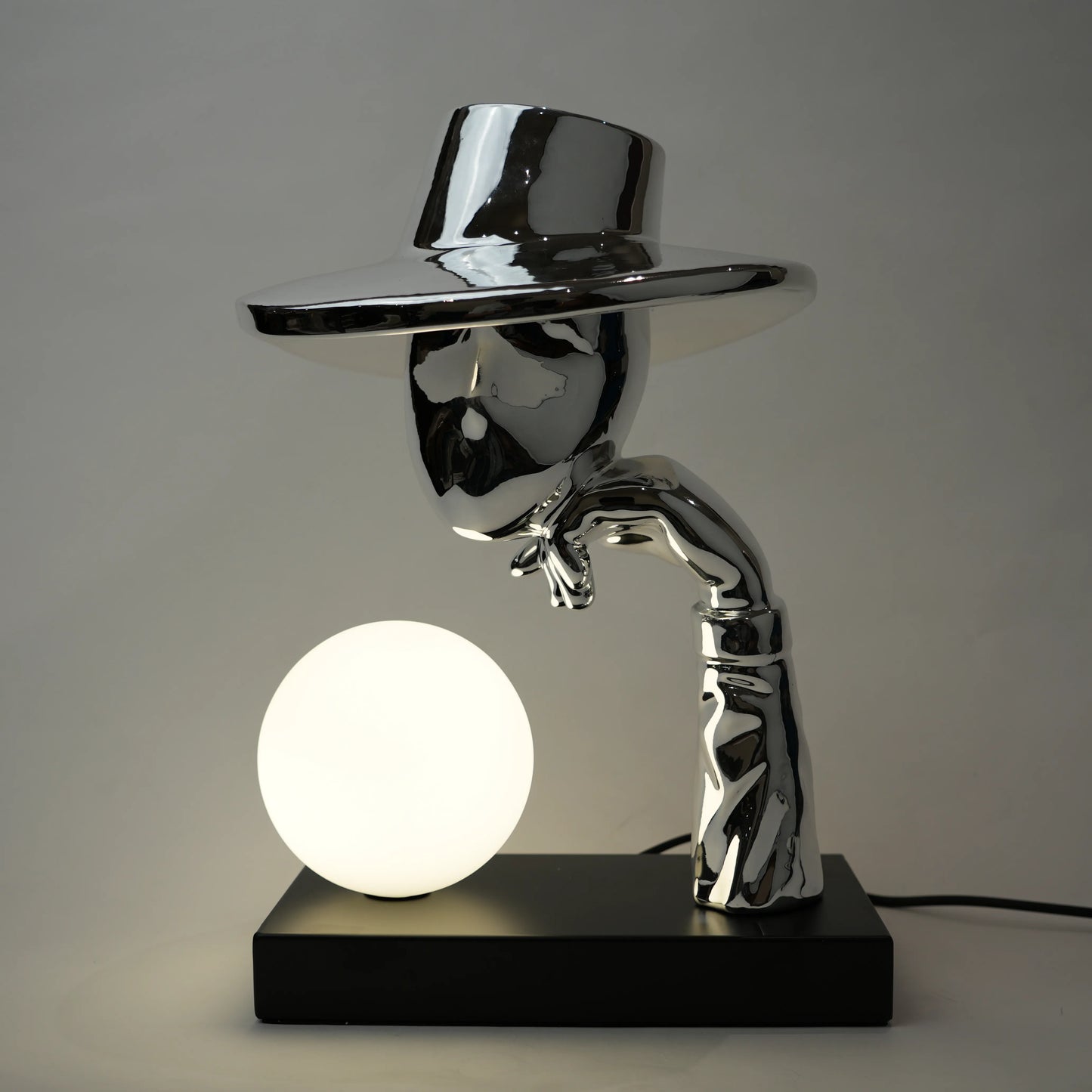 Decorative lamp with a metallic top hat and arm holding a light bulb on a gray background