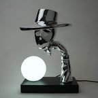 Metallic sculpture of a figure holding a glowing sphere on a black base against a gray background