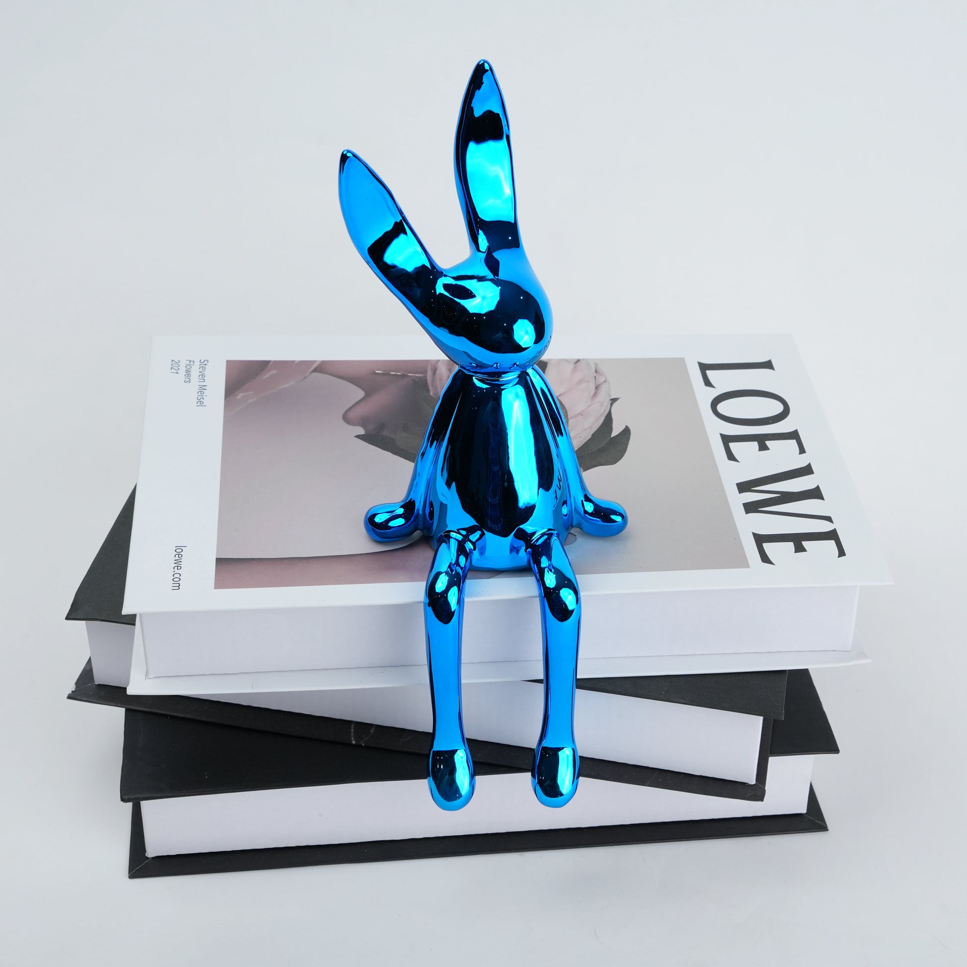 Resin bunny figurine with elongated ears and a minimal seated design, featuring smooth contours and extended legs for edge placement, available in matte and reflective electroplated finishes.