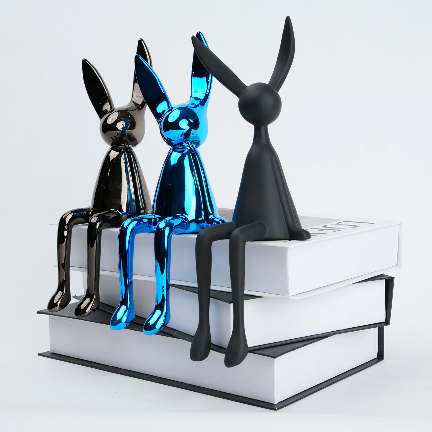 Three metallic dog figurines in black, blue, and black sitting on a stack of books.