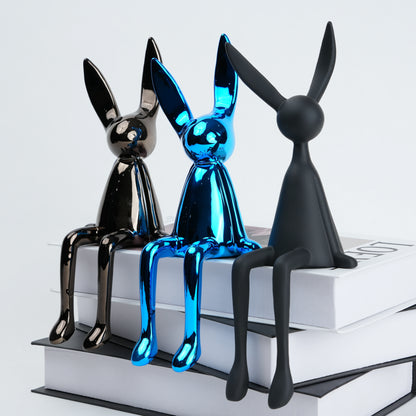 Three metallic rabbit figurines in black, blue, and silver on a white surface.