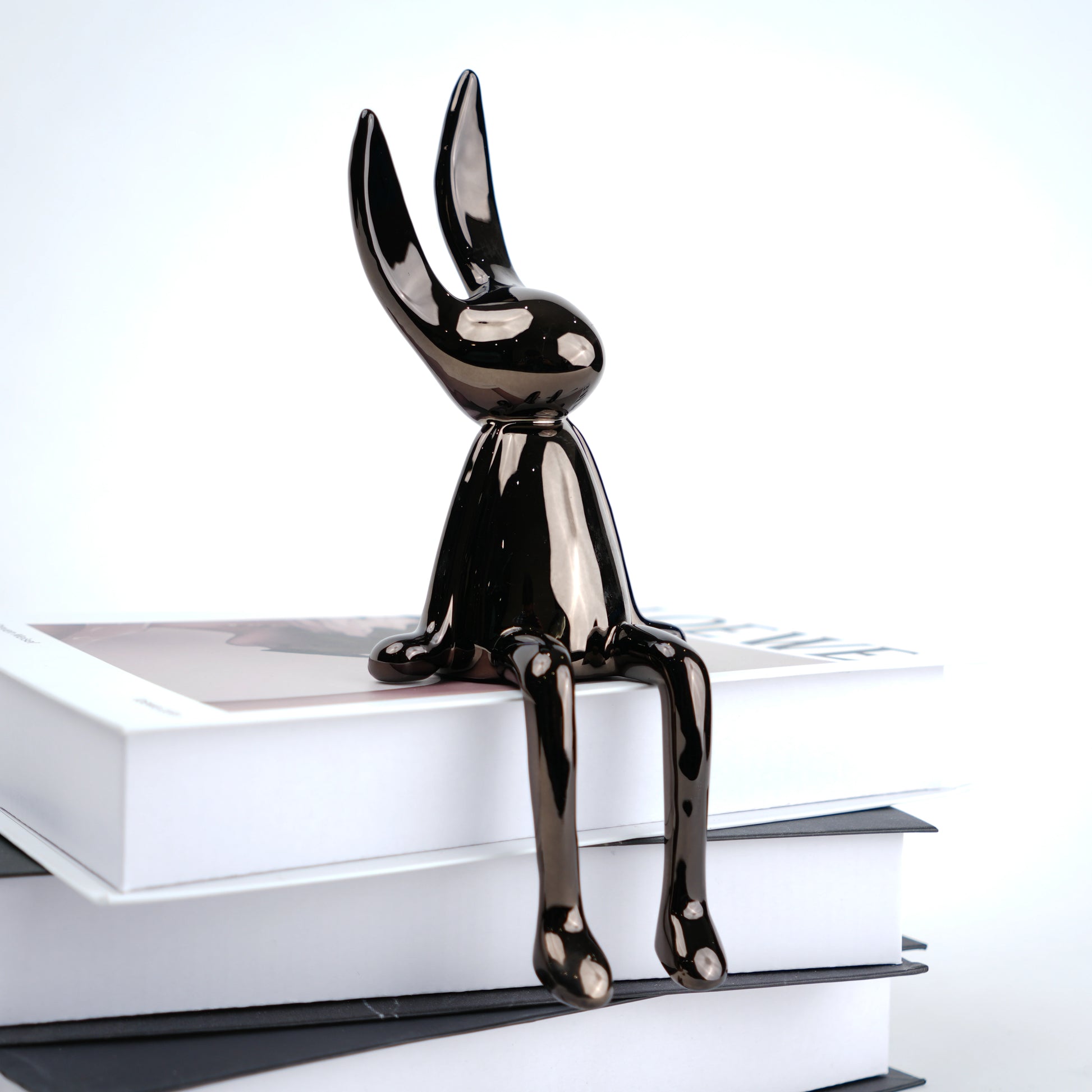 Black rabbit-shaped figurine on a stack of books with a white background