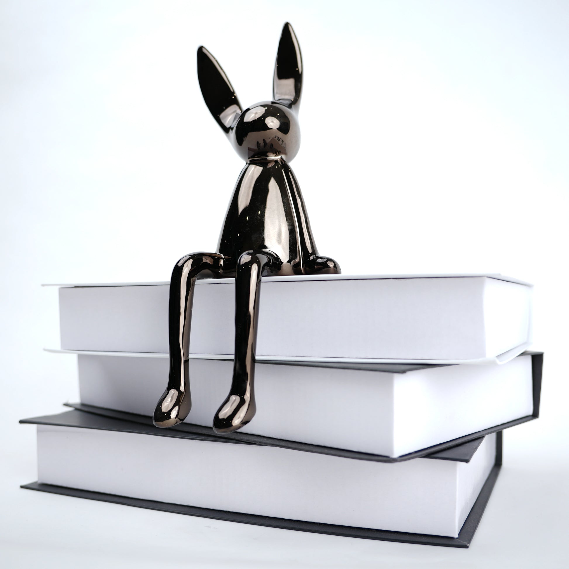 Metallic dog figurine sitting on a stack of books against a white background