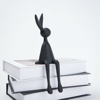 Black rabbit figurine sitting on a stack of books with a white background