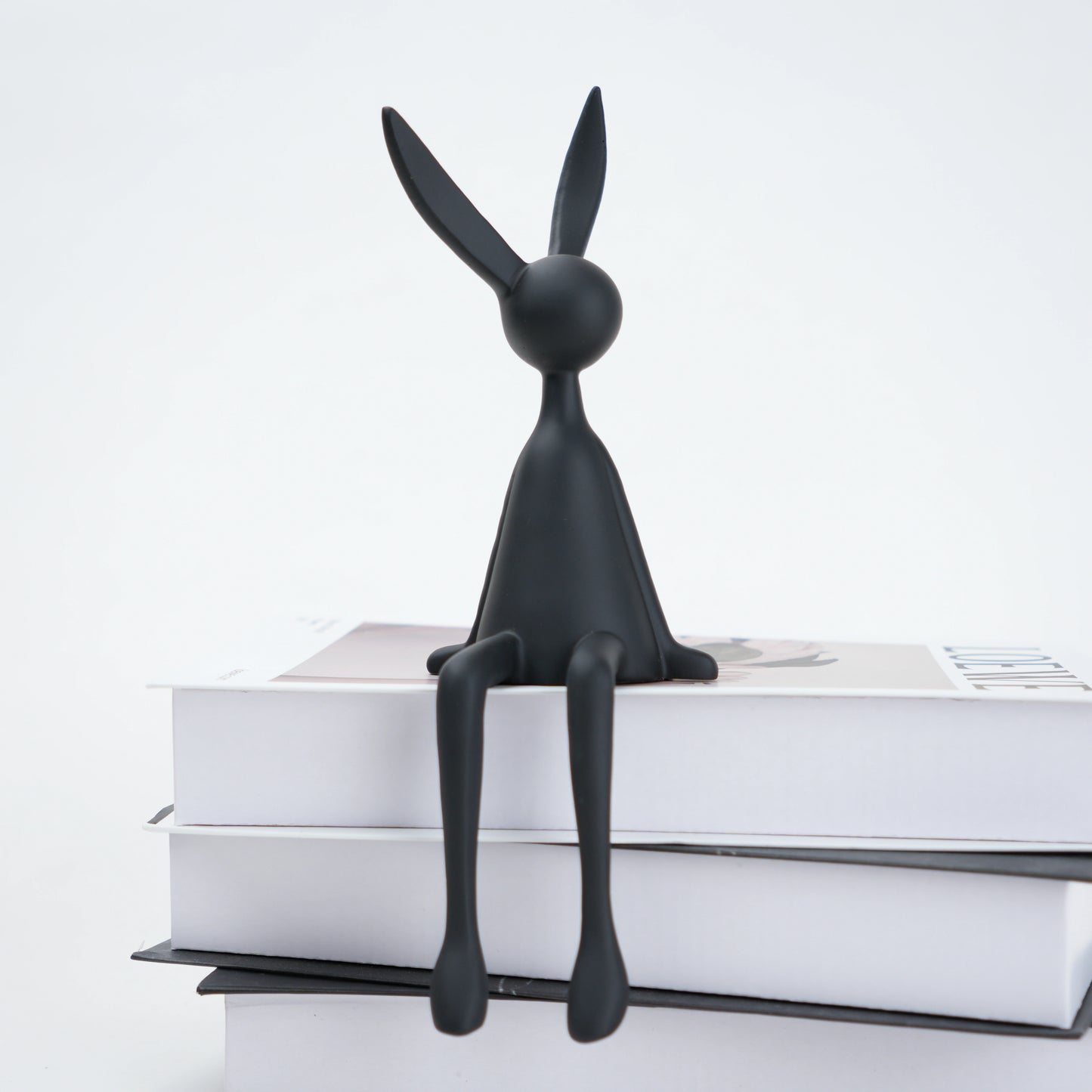 Black rabbit-shaped bookend on a stack of books with a white background