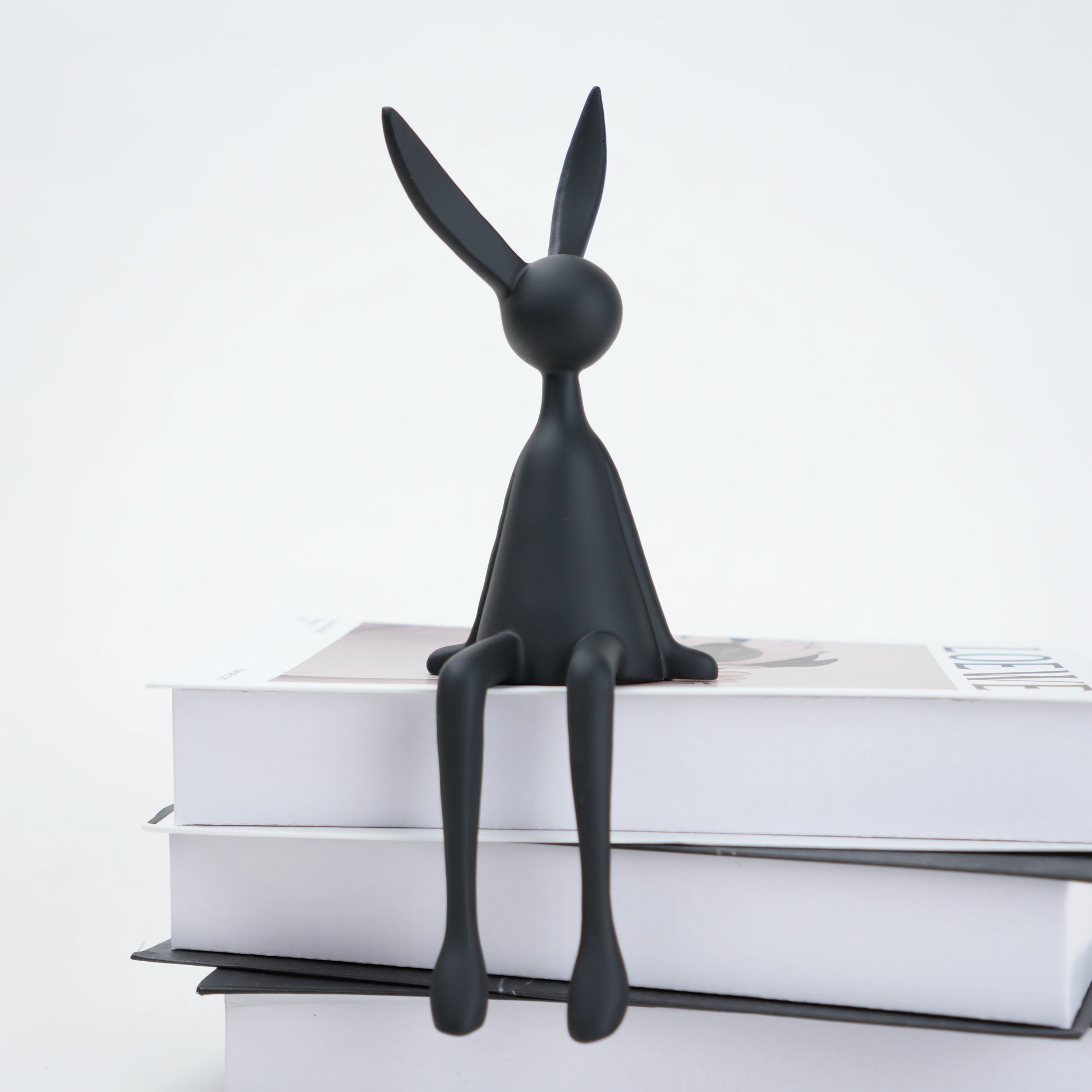 Black rabbit-shaped bookend on a stack of books with a white background